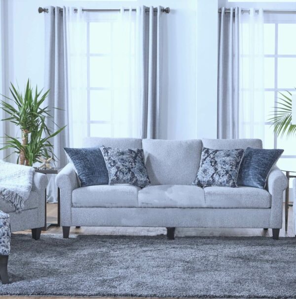 Reedy couch with four pillows on a rug in front of two tall windows