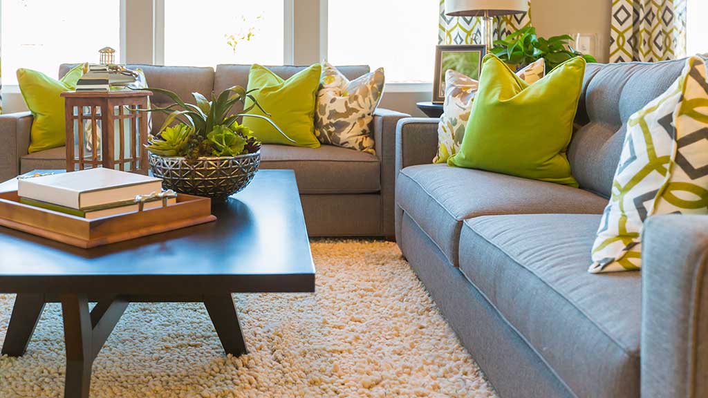 Furnished living room with grey couches, a coffee table, and green accent pillows